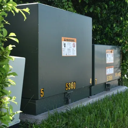 a typical 1m tall green power transformer box sits on a patch of grass.