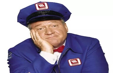 A grey-haired man in a blue uniform with Maytag on the police-style hat sits looking bored.